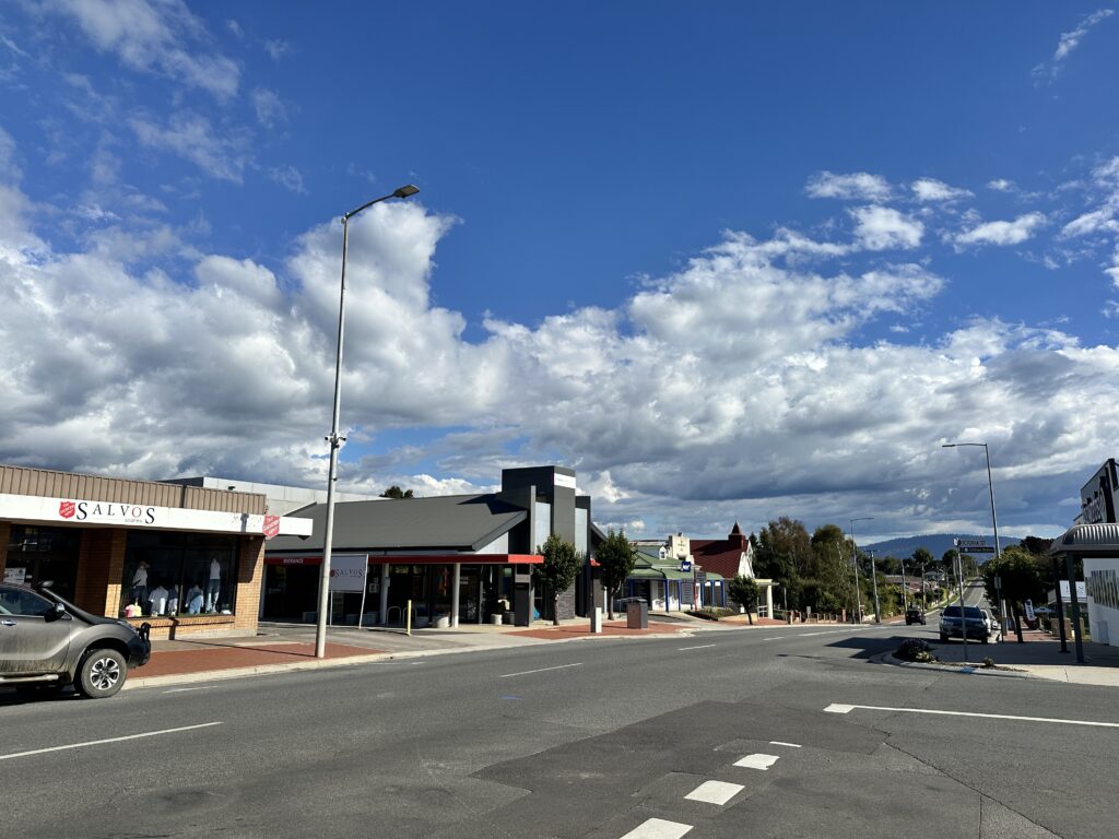 A quiet small-town street with shops under a blue sky with scattered clouds