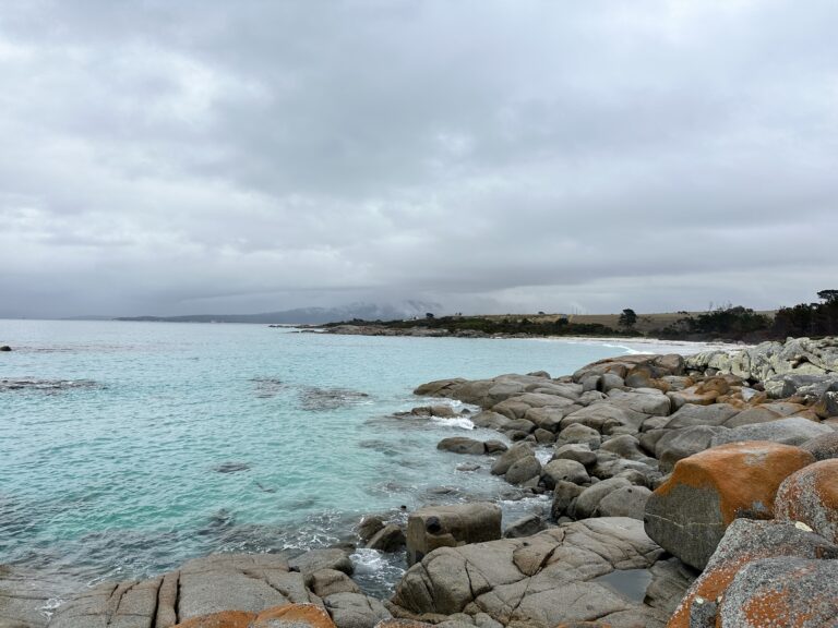 A rocky shoreline with clear turquoise water under a cloudy sky